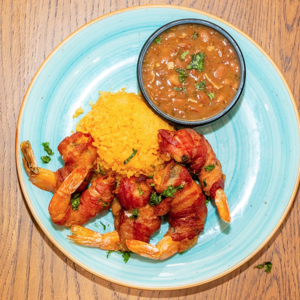 Plate of bacon-wrapped shrimp with yellow rice and a bowl of tomato salsa on a turquoise plate.