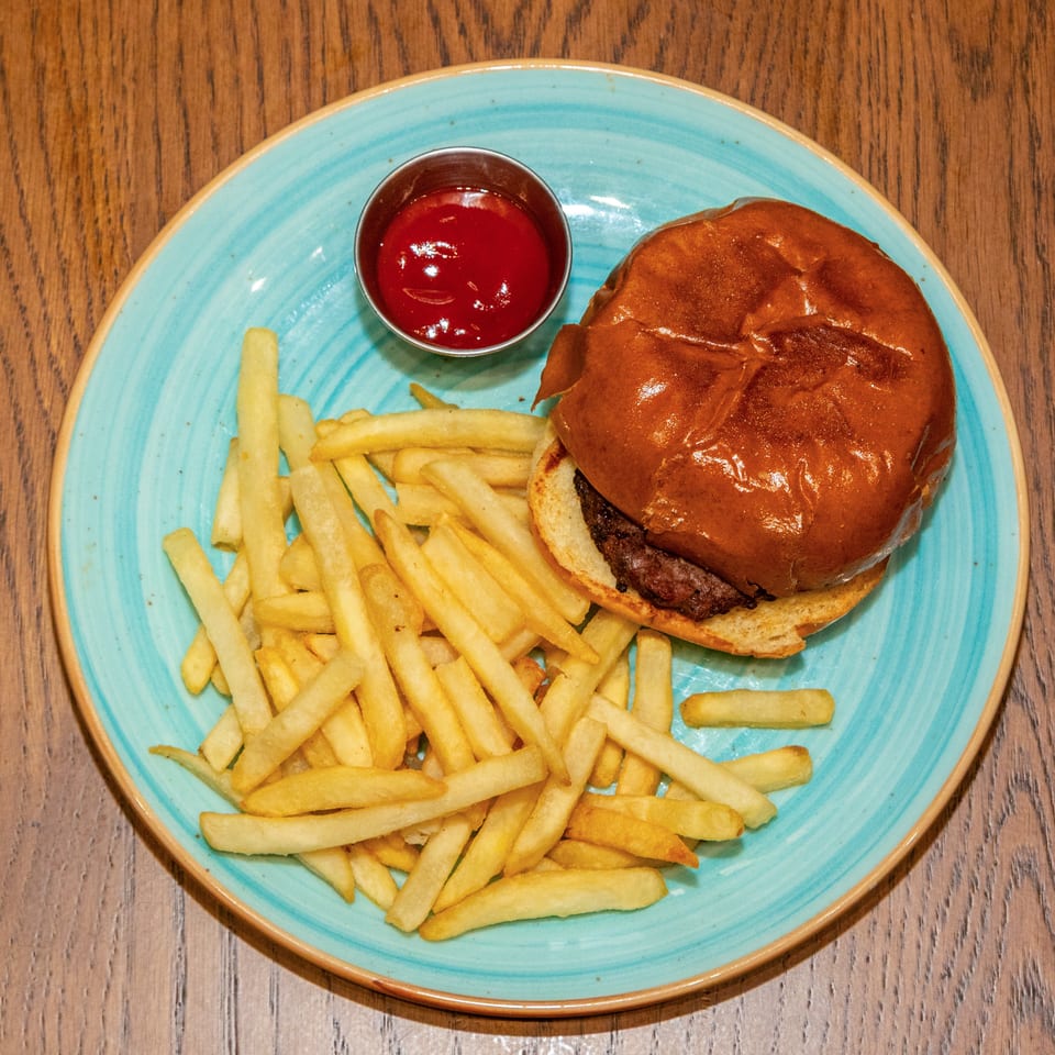 Burger with a glossy bun, French fries, and ketchup on a turquoise plate atop a wooden table.