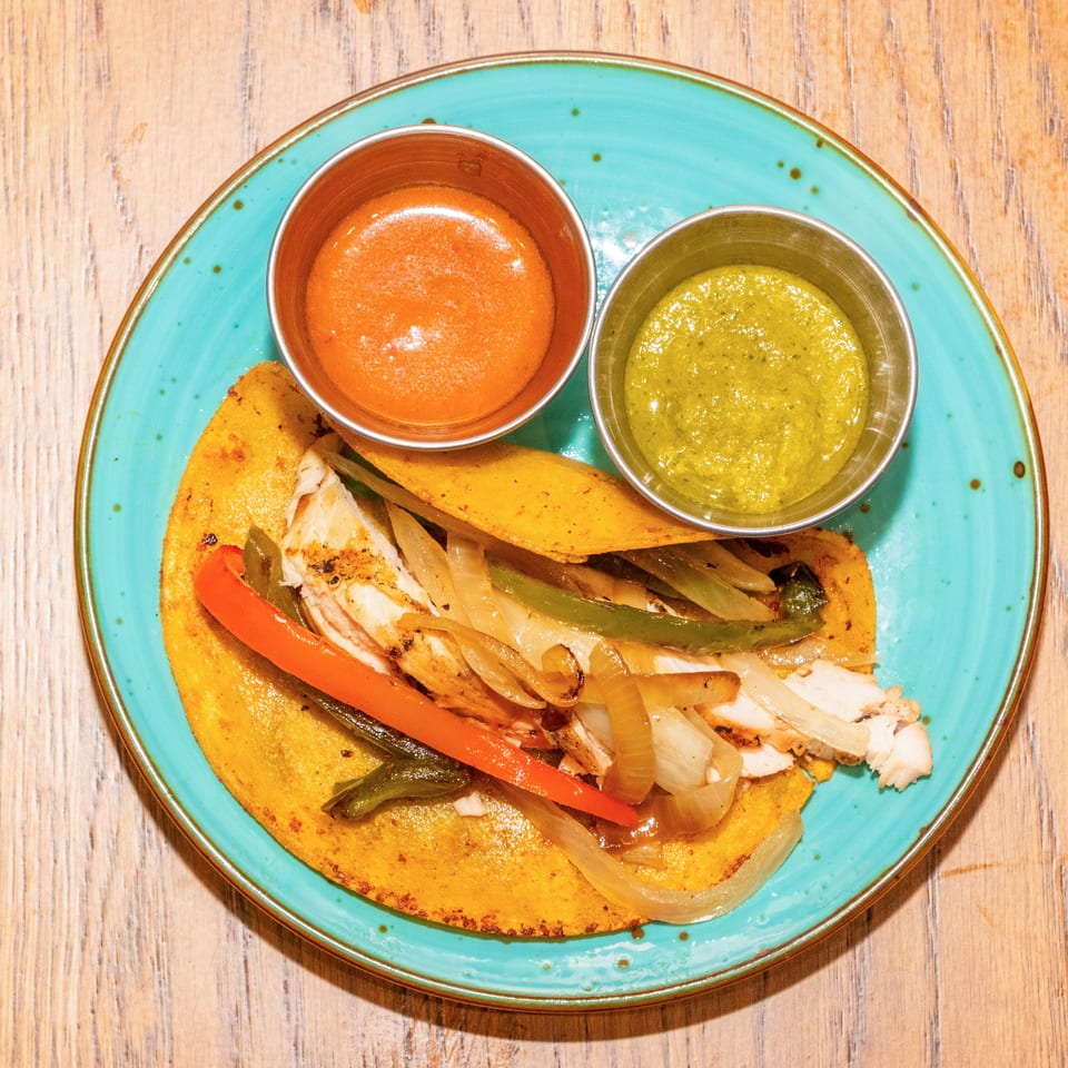 Overhead view of grilled chicken tacos with sautéed onions and peppers, served with red and green sauces on a turquoise plate.