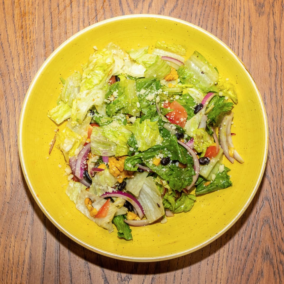 Overhead view of a colorful garden salad with lettuce, tomatoes, black beans, corn, red onions, and crumbled cheese in a yellow bowl.