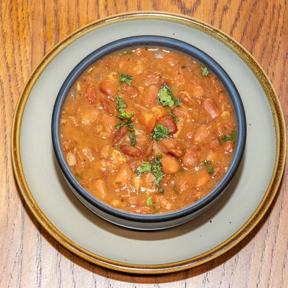 Bowl of tomato-based bean stew garnished with fresh cilantro, set on a ceramic plate atop a wooden table.