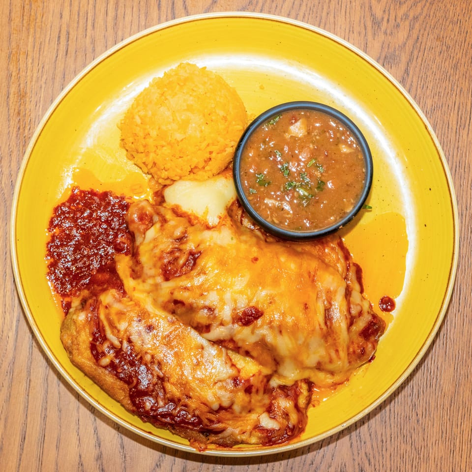 Cheesy enchiladas with Spanish rice, refried beans, potatoes, and a bowl of salsa on a yellow plate.