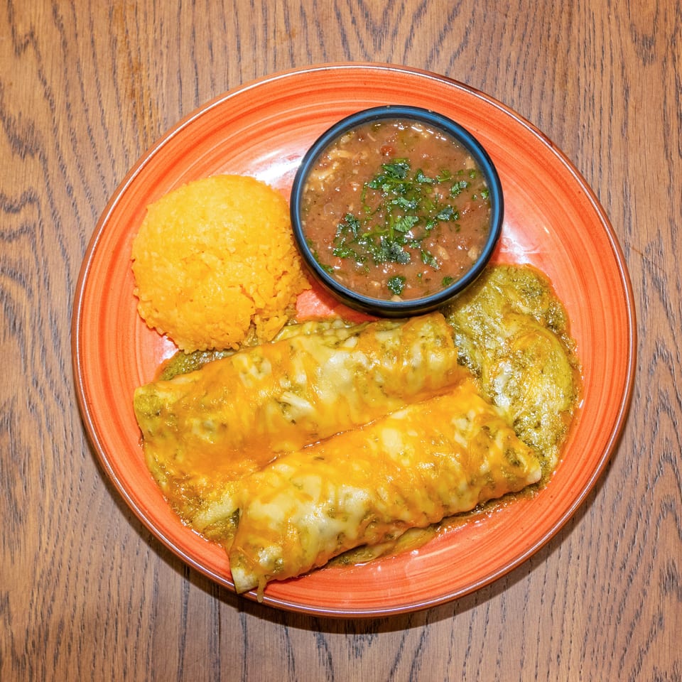 Cheesy enchiladas with orange rice and herb-topped beans served on an orange plate over a wooden table.